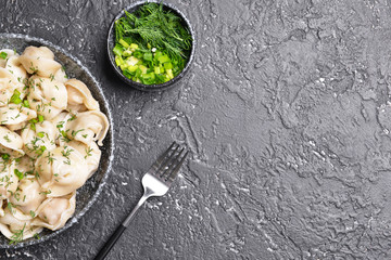 Bowl with tasty dumplings and herbs on dark background