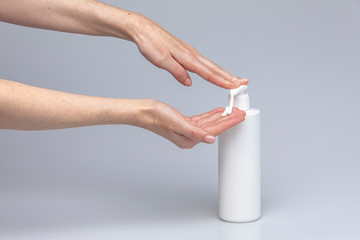 White people's hands using white body cream isolated in front of a grey background with structurant lights and shadows