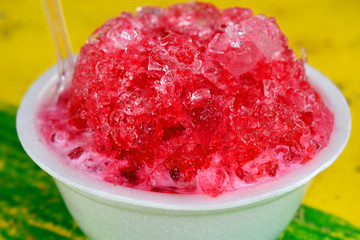 Close-up on Sweet shaved ice  in foam cup on colorful of yellow- green table. Famous Thai dessert in Summer.