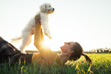 Beautiful young caucasian girl playing with her dog lying on the grass in the park at sunset....