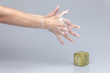 White people's hands washing each other with green foamy 
Marseille's soap isolated in front of a grey background with structurant lights and shadows