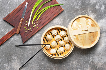 Steamer with tasty dumplings and green onion on grey background