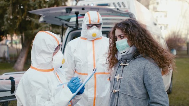 People with protective suits helping woman outdoors, coronavirus concept.
