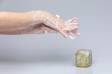 White people's hands washing each other with green foamy 
Marseille's soap isolated in front of a grey background with structurant lights and shadows