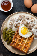 Beige plate with potato waffle, champignons, fried egg and pickles. Close-up, vertical shot, top view
