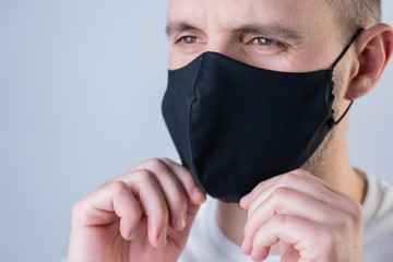 Man puts on a face mask. Black stylish face mask during a pandemic virus crown. Handmade cotton...
