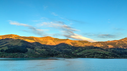 The rising sun lights up the tips of the mountains surrounding Akaroa Harbour on Banks Peninsula, New Zealand