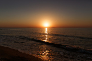 Sea coast at sunset, with the sun, wave, orange sky