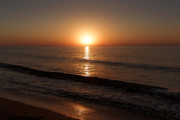 Fototapeta na wymiar Sea coast at sunset, with the sun, wave, orange sky