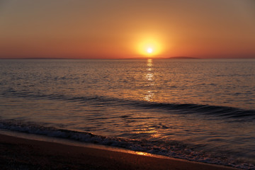 Sea coast at sunset, with the sun, wave, orange sky