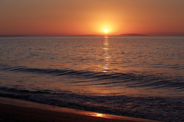 Fototapeta na wymiar Sea coast at sunset, with the sun, wave, orange sky