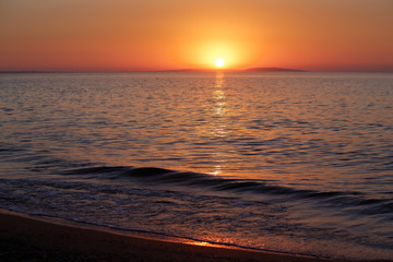 Sea coast at sunset, with the sun, wave, orange sky