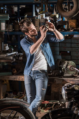 A young man with a hipster look works in his workshop repairing vintage motorcycles.