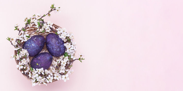 Violet easter eggs in a basket with flowers on a pink background. Horizontal photograph. Top view