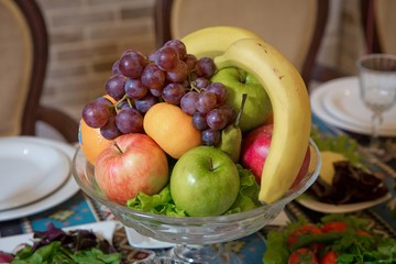 Fruit in a bowl .Red and blue apple, orange, red banana banana. Cucumber, tomato, greens, radish.