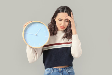 Worried woman with clock on grey background. Time management concept