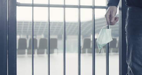 Man holds in hand protective face mask at an empty football stadium closed for safety isolation and social distance due to contagious coronavirus covid 19 infectious pandemic outbreak - Powered by Adobe
