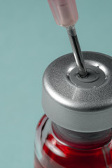 Medical needle pierces the cap of medical jar with red liquid, macro