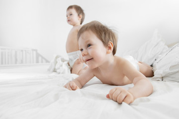 Small twins emotional play on bed. Babies twins sit down in Bed. Fashion image of baby and family