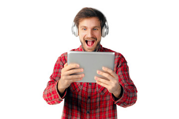 Shoot of young caucasian man using tablet and headphones isolated on white studio background. Concept of modern technologies, gadgets, tech, emotions, advertising. Copyspace. Crazy happy, surfing.