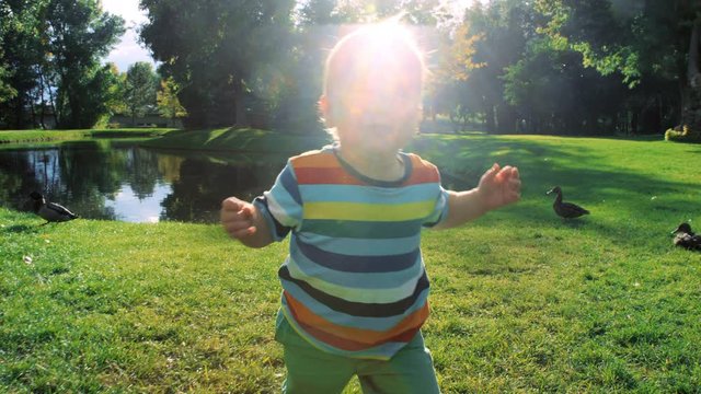 Adorable toddler boy charges at camera while leaving duck pond slow motion