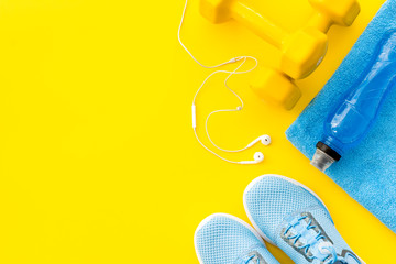 Fototapeta na wymiar Fitness equipment. Sneakers, towel, water on yellow background top view copy space
