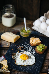 Fried egg with parmesan and toast with cream cheese and avocado paste on black plate, top view