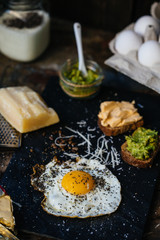 Fried egg with parmesan and toast with cream cheese and avocado paste on black plate, top view