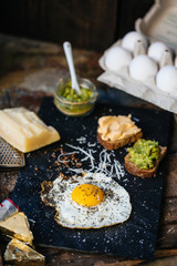 Fried egg with parmesan and toast with cream cheese and avocado paste on black plate, top view