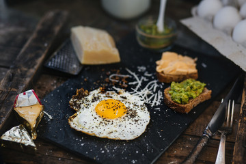 Fried egg with parmesan and toast with cream cheese and avocado paste on black plate, top view