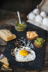 Fried egg with parmesan and toast with cream cheese and avocado paste on black plate, top view