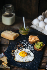 Fried egg with parmesan and toast with cream cheese and avocado paste on black plate, top view