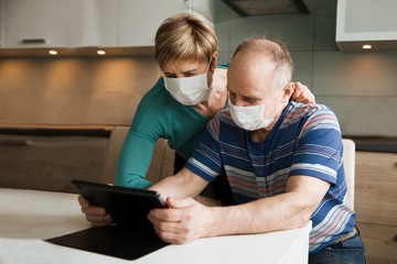Seniors couple  wearing medical face mask and using tablet at home. quarantine. Corona Virus. order of products online and communicates on the Internet  at home. stay home concept
