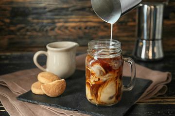 Pouring of milk into cold coffee in mason jar on table