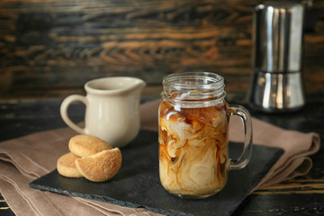 Mason jar of tasty iced coffee with cookies on wooden background