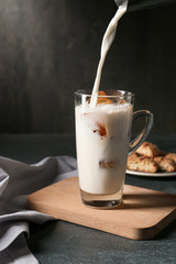 Pouring of milk into cold coffee in glass cup on dark background