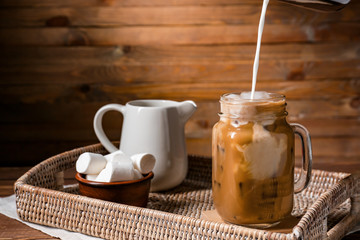 Pouring of milk into cold coffee in mason jar on tray