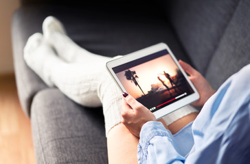 Woman watching tv series or movie stream with tablet on couch wearing cozy long socks. Girl...