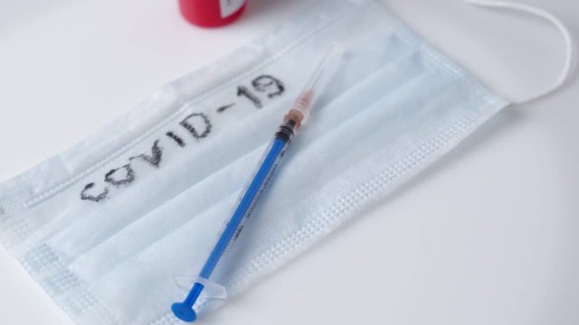 A medical mask, a syringe and a test tube with blood rotates on a white background. The Inscription Covid 19