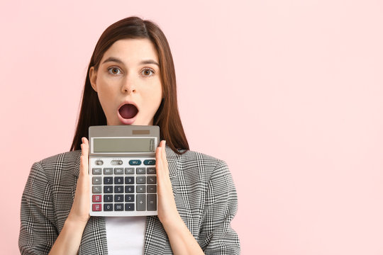 Shocked young woman with calculator on color background