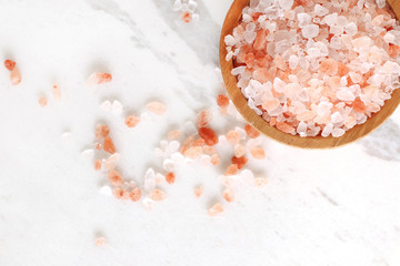 top view of himalayan pink rock salt in wooden bowl on white marble table with copy space. - obrazy, fototapety, plakaty