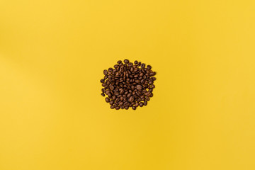A handful of coffee beans in the center of the frame on a yellow background