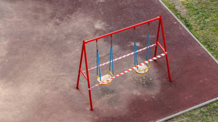 Empty children's swing in the playground tied with white and red striped tape