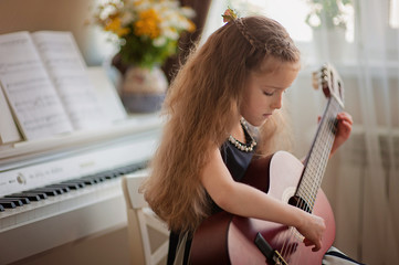 Home lesson on music for a girl with a guitar and piano. The idea of activities for the child at home during quarantine