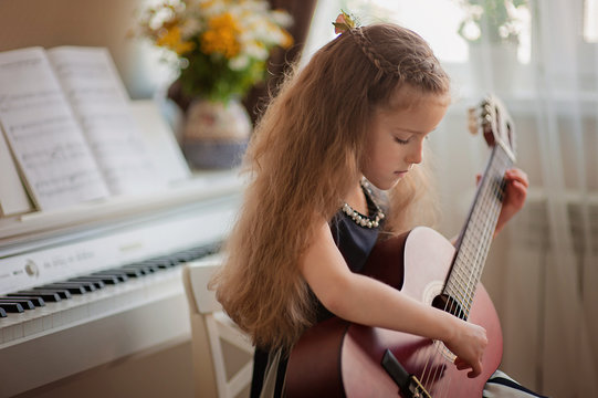 Home lesson on music for a girl with a guitar and piano. The idea of activities for the child at home during quarantine