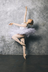 Fototapeta na wymiar Pretty young ballerina dancer dancing classical ballet against rustic wall