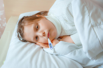 a young girl is lying in bed ill with a thermometer