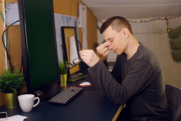 Fototapeta premium Stay at home, a man works at home. Freelance, a man studying a new program, online. A man with glasses sits at home at a computer; his eyes hurt. Computer vision problems