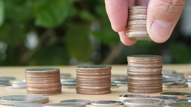 Saving money hand putting coins on stack on table with sunshine on nature background.