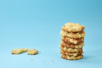 Pieces of broken biscuits on the left from cheese cookies, placed on top of each other, like a pyramid, isolated on light blue background. Nutritious snack.